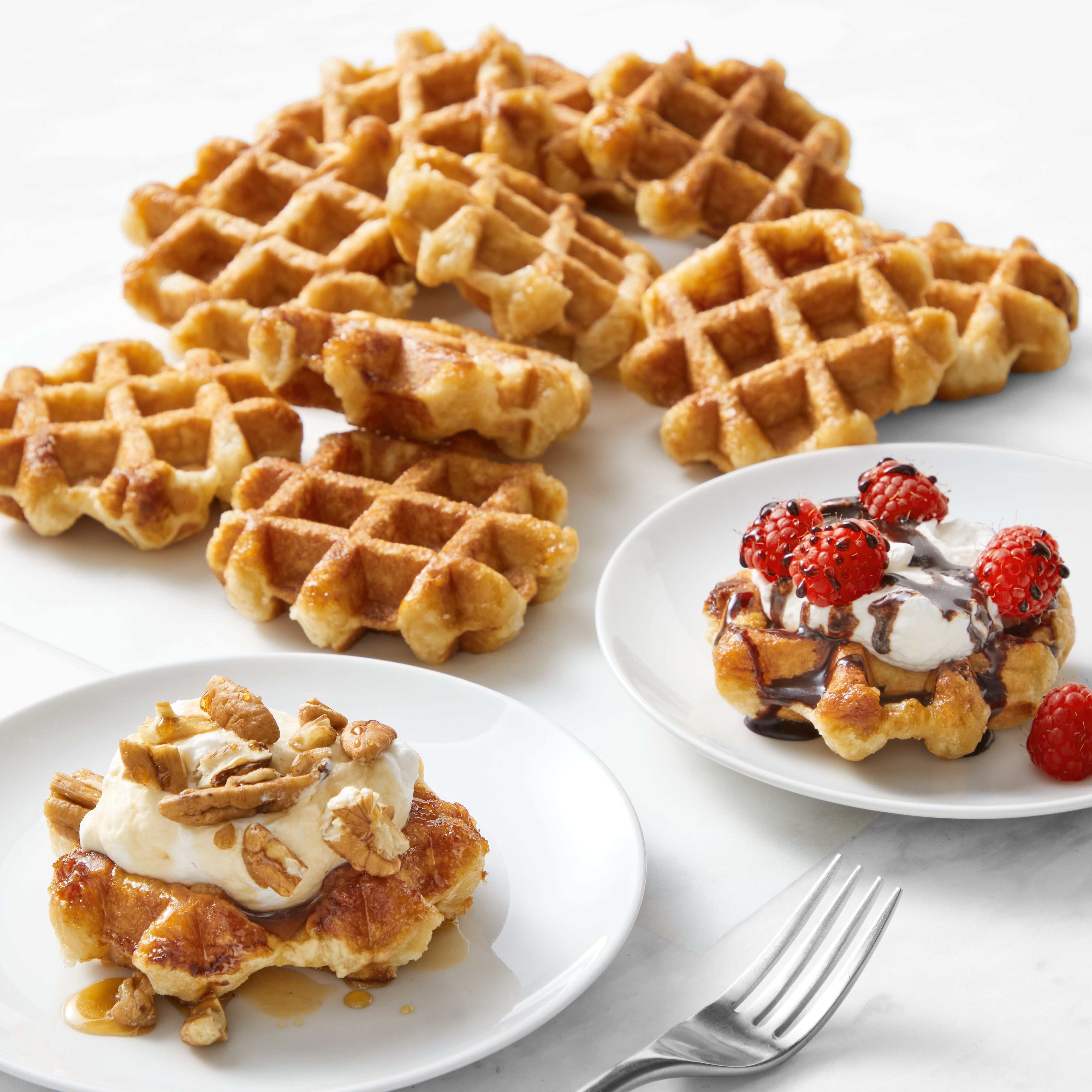 Four plates of waffles: one topped with nuts, bananas, syrup; another with berries, cream, chocolate.